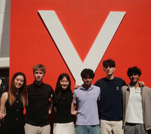 Evan and five others in bright sunlight in front of a large white letter Y mounted on a red LED wall