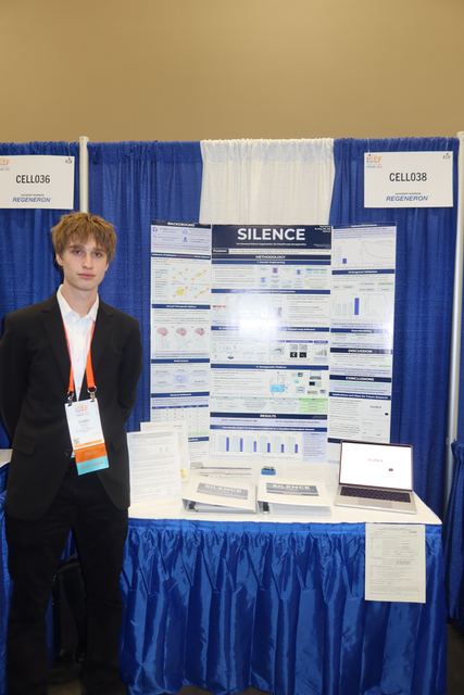 Full view of Evan standing beside his complete CELL038 SILENCE booth, with the CELL036 and CELL038 signs, poster, handouts, binders, and laptop on the blue-skirted table