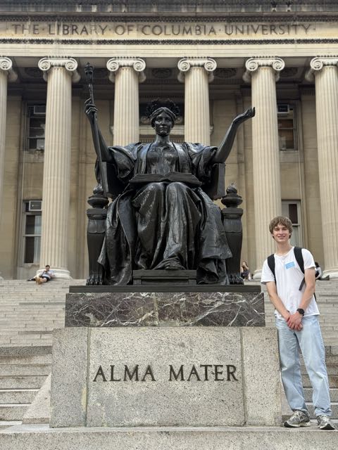 Evan standing beside the bronze Alma Mater statue on the library steps at Columbia University