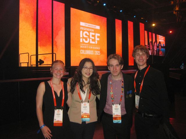 Four students pose in front of the Regeneron ISEF Columbus 2025 awards-stage screen; two wear medals, Evan is the tall blond student at right