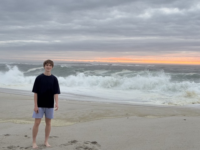 Evan on an empty beach at dawn, heavy surf breaking behind him under an orange band of sunrise