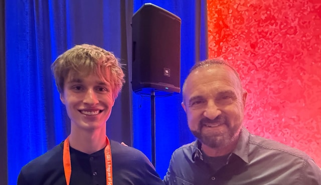 Evan Morris, wearing his finalist lanyard, with a smiling man in front of blue stage curtains and a red backdrop at Regeneron ISEF 2026 in Phoenix