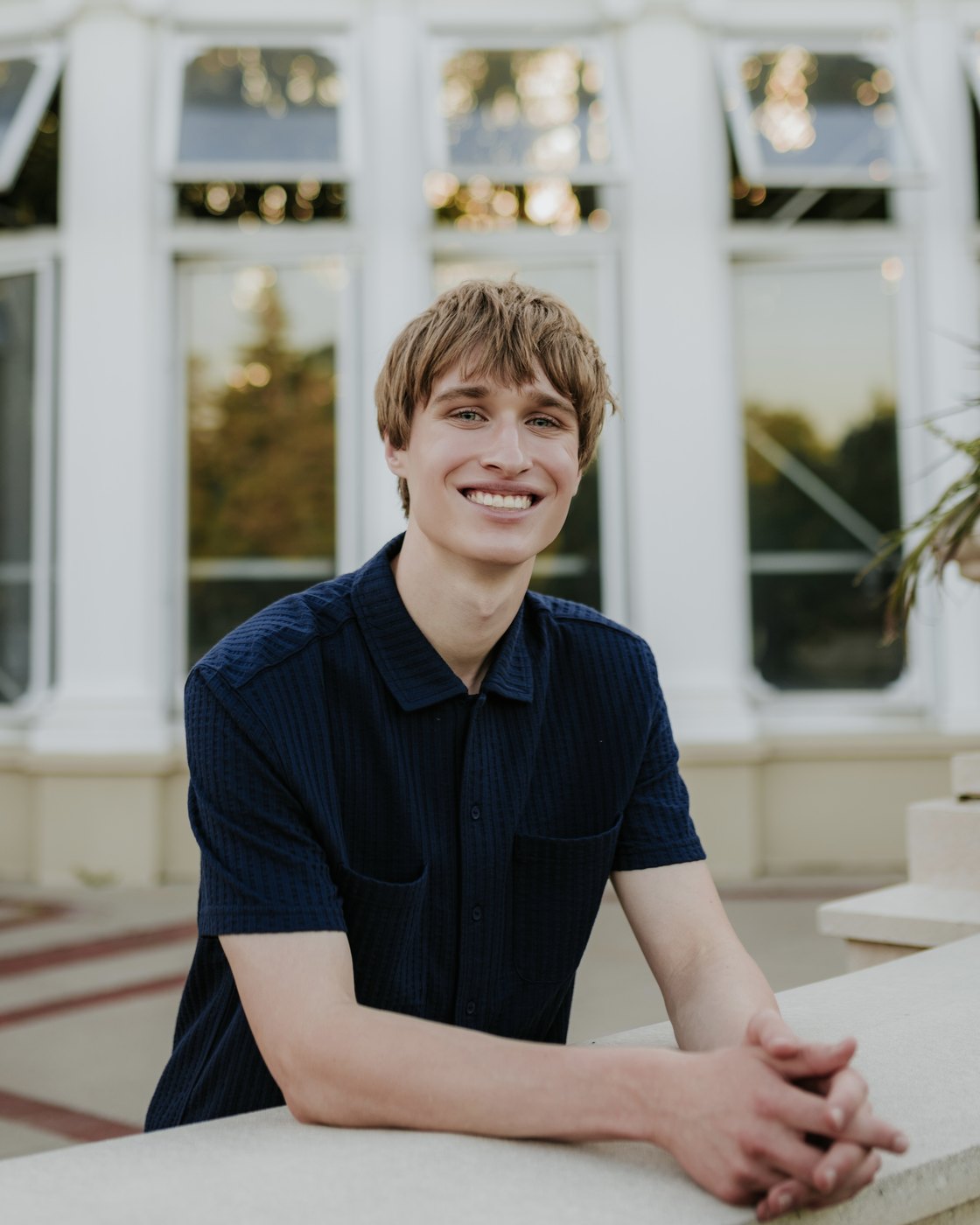 Evan Morris smiling, leaning on a stone ledge in front of a white conservatory