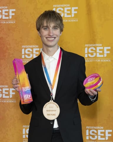 Evan Morris backstage at Regeneron ISEF 2026, wearing the first-place medal and holding his trophy and award disc