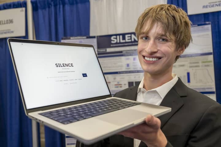 Evan Morris holding an open laptop showing the SILENCE software, in front of his research poster at Regeneron ISEF 2026
